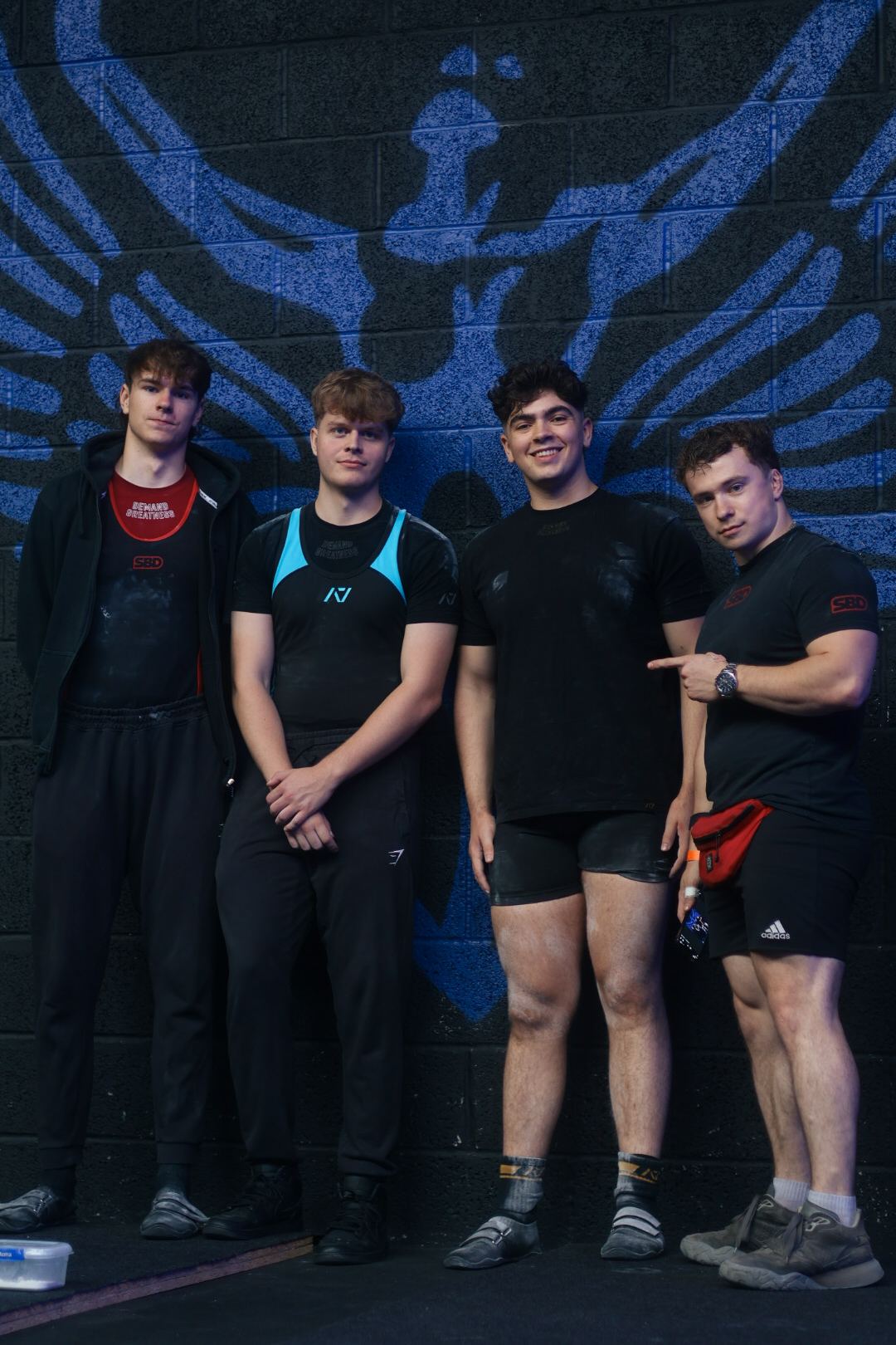 Coach with three lifters in front of a blue mural