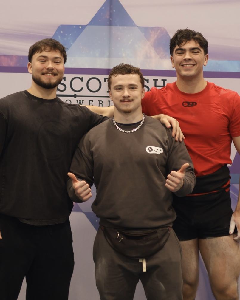 Coach with two lifters in OSP gear at a Scottish Powerlifting championship